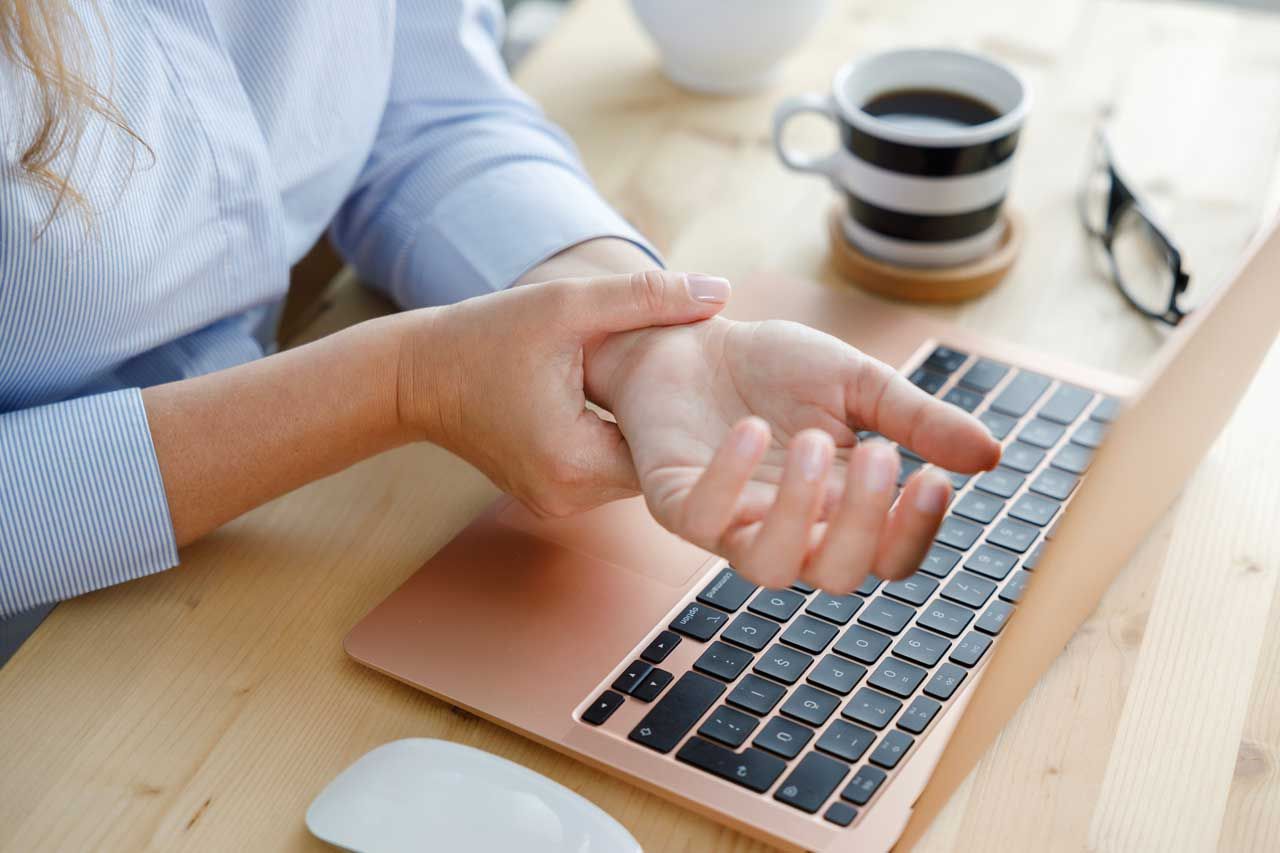 Frau hält schmerzendes Handgelenk am Laptop – mögliches Karpaltunnelsyndrom durch Büroarbeit