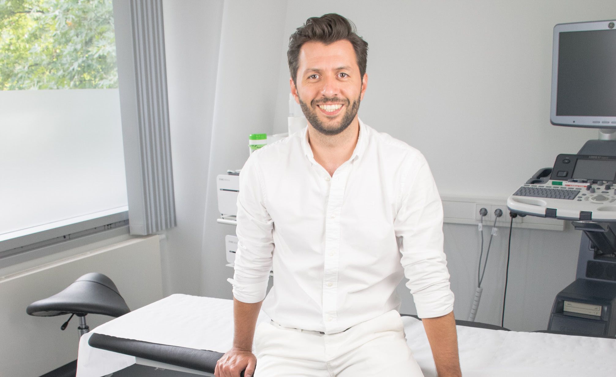 Dr. Christoph Bauer sitzt auf einer Liege in seinem modernen Behandlungsraum.